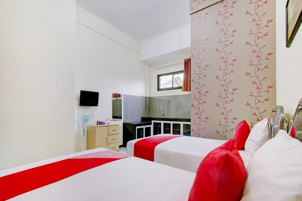 Ein Hotelzimmer mit zwei Betten, einer Küchenzeile, einem Fernseher und einem Fenster mit Vorhängen.