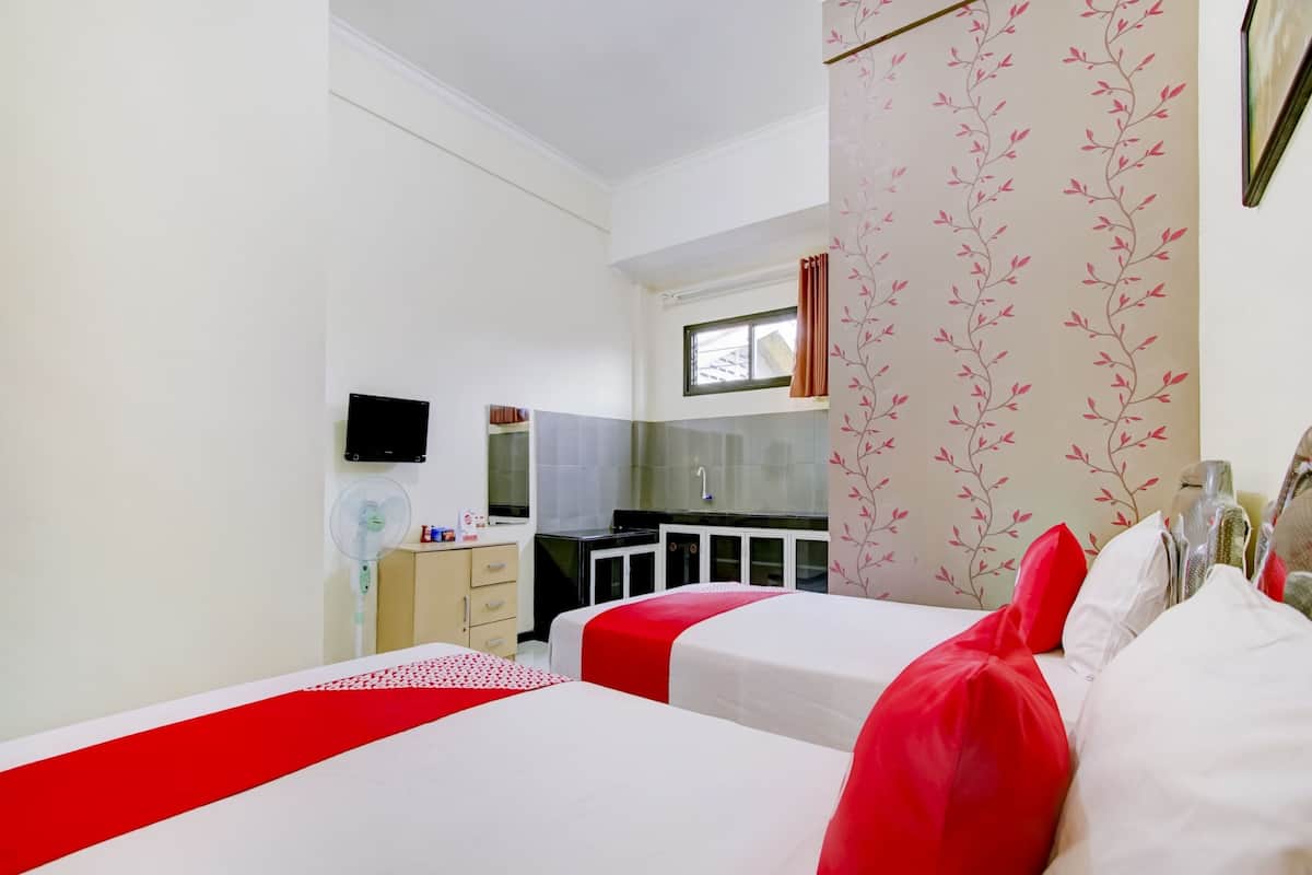 Hotellihuone, jossa on kaksi sänkyä, pieni keittiö, televisio ja ikkuna, jossa on verhot.
