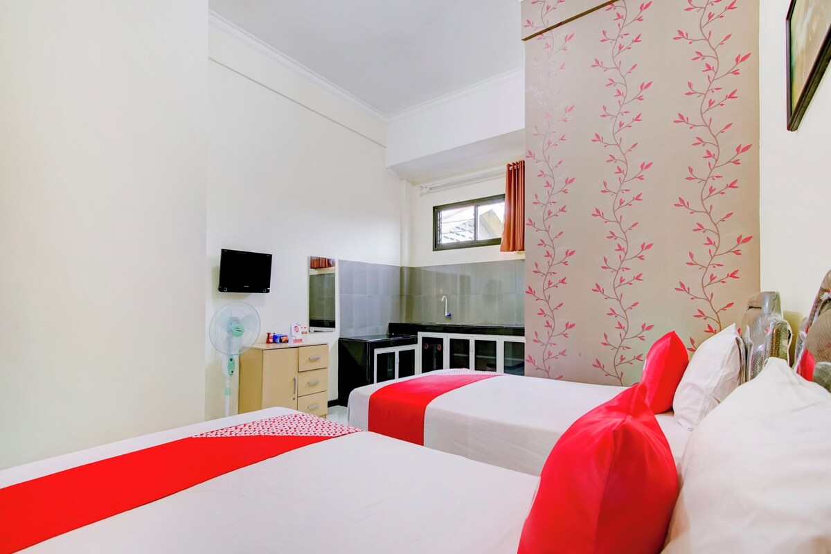 A hotel room with two beds, a kitchenette, a TV, and a window with curtains.