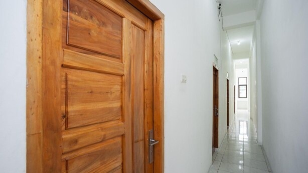 Una puerta de madera con manija de metal en un pasillo con paredes blancas y suelo de baldosas.