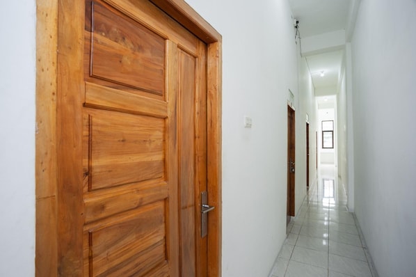 A wooden door with a metal handle in a hallway with white walls and a tiled floor. - OYO 3929 8angau Mas (Palembang)