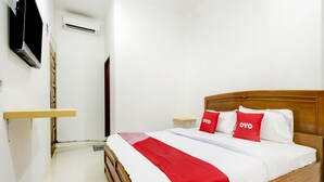 Habitación de hotel ordenada con cama de madera, ropa blanca y detalles en rojo.