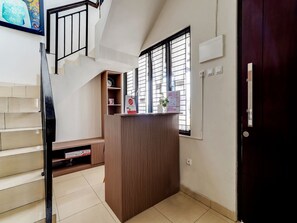 A reception desk with a wooden finish, a staircase with beige steps, and a window with blinds.