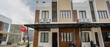 Um edifício moderno de dois andares, com telhado plano, várias unidades de ar condicionado e uma área de entrada coberta.