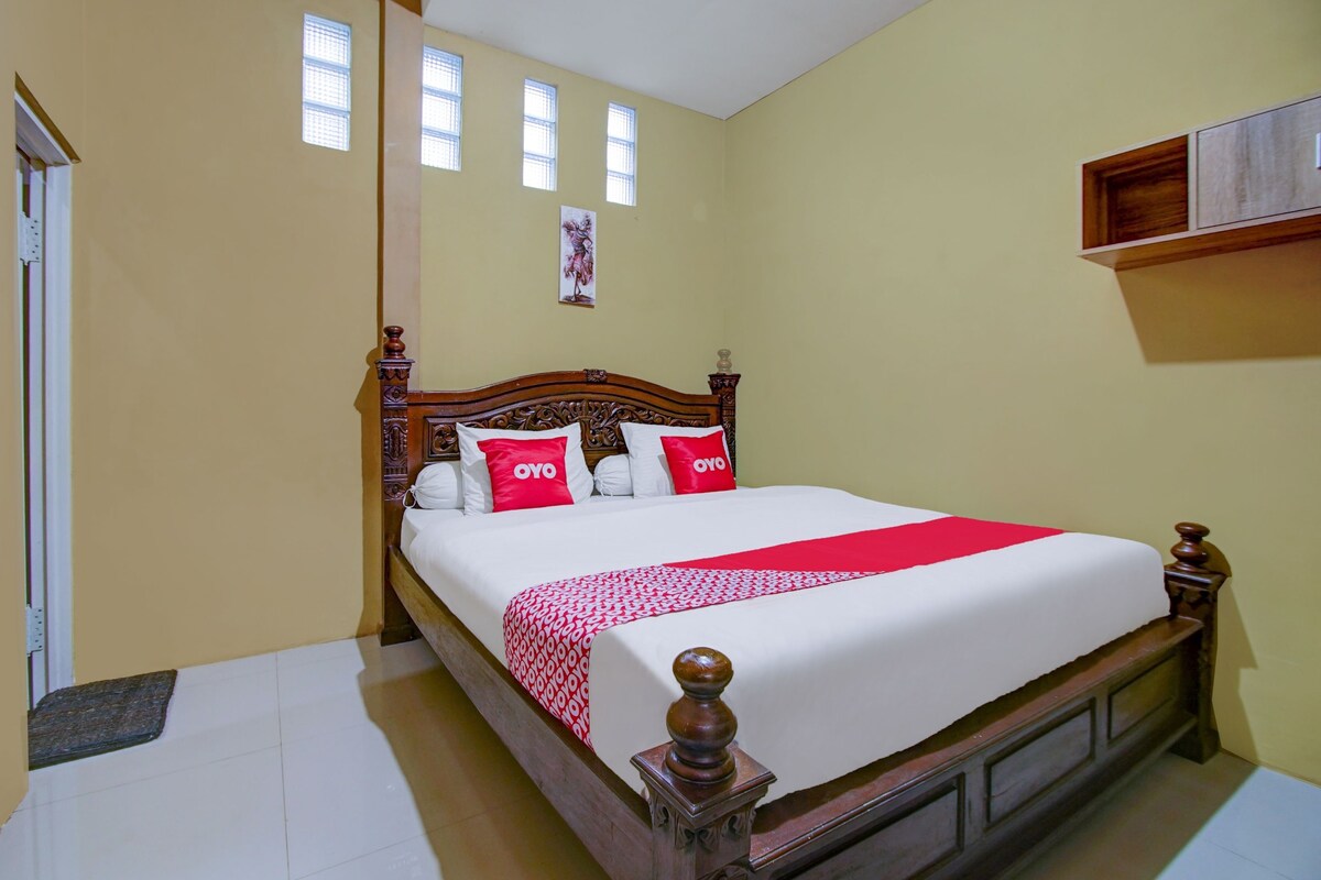 A hotel room with a wooden bed, a red and white bedspread, and a single window with blinds.