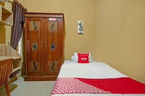 A bedroom with a bed, a wooden wardrobe, a desk, and a red pillow with 'OYO' branding. - OYO 90061 Melati House Syariah (Kepanjen)