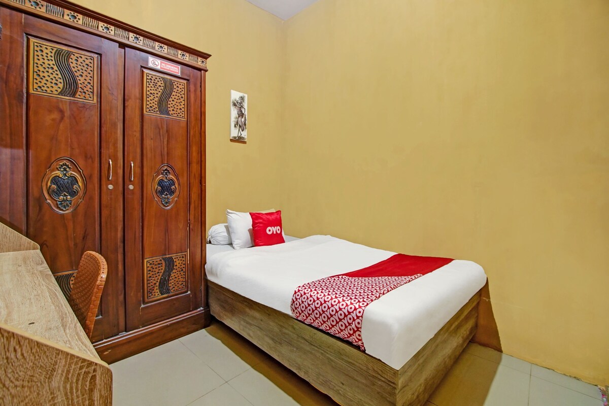 A hotel room with a wooden wardrobe, a bed with a red and white blanket, and a small table.