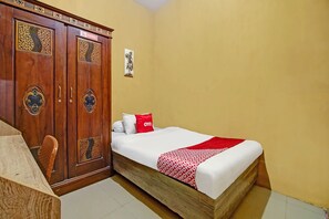 A hotel room with a wooden wardrobe, a bed with a red and white blanket, and a small table. - OYO 90061 Melati House Syariah (Kepanjen)