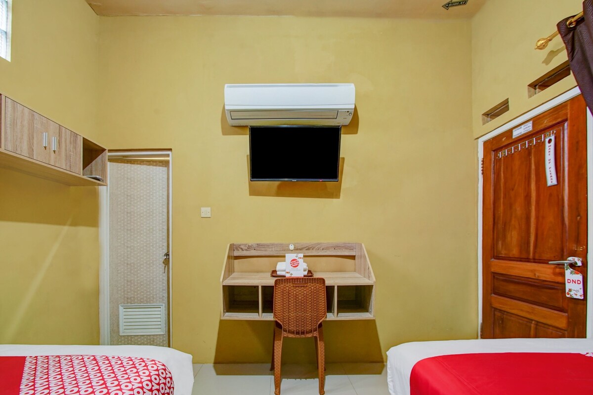 A room with two beds, a desk with a chair, a television, and an air conditioning unit.