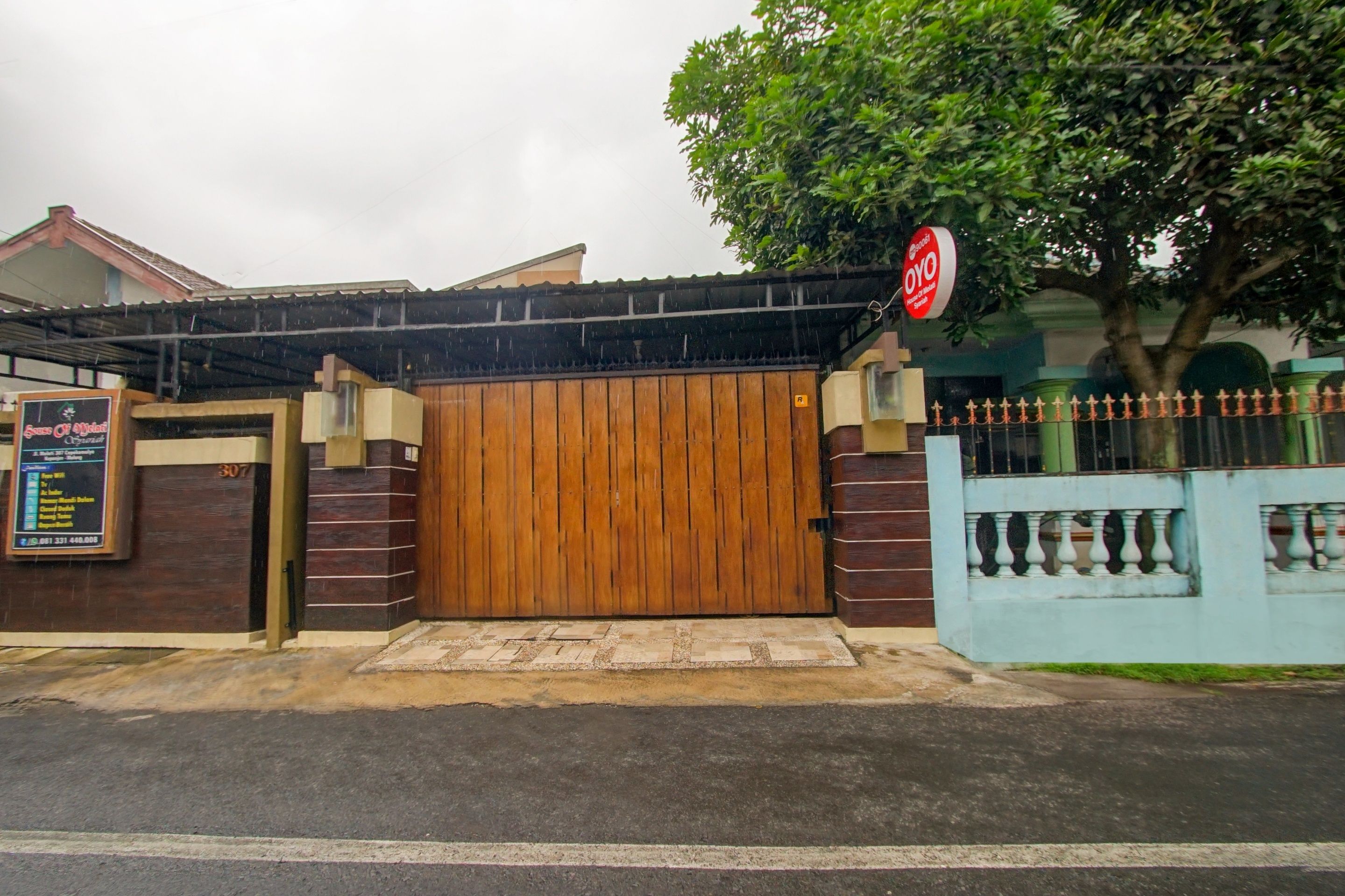 A gated entrance with a wooden door, a signboard, and a tree.