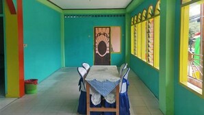 A room with a table set for four, a door with a decorative design, and windows with yellow frames. - Hotel Sinar Lumayan Syariah (Balikpapan)