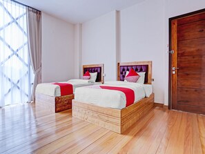 A hotel room with two wooden beds, a large wooden door, and a window with sheer curtains.