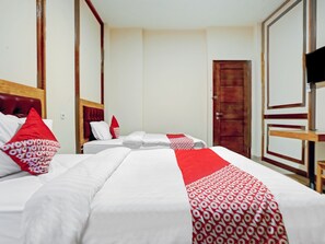 A hotel room with two beds, one with a red and white patterned bedspread and the other with plain white bedding. There is a wooden headboard and a wooden wardrobe with a mirror.