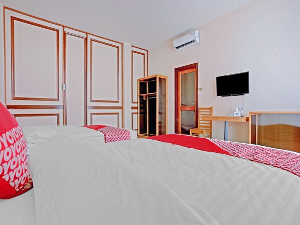 A hotel room with two beds, a desk, a chair, a TV, and an air conditioning unit.