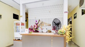 A reception desk with a white backdrop, a fan, and floral arrangements. - OYO 90052 Star House (West Cirebon)