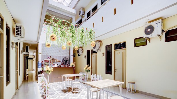 A spacious indoor area with a checkered floor, a central table with chairs, and hanging plants. - OYO 90052 Star House (West Cirebon)
