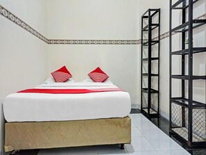 Un lit avec une literie blanche et des oreillers rouges, une base de lit de couleur beige et une bordure à motifs sur le mur.