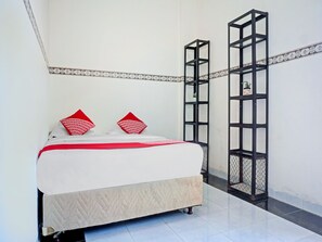Un lit bien fait, recouvert d’une couvre-lit blanche et rouge, avec deux oreillers rouges et une bordure décorative sur le mur.