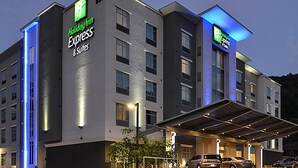 Een Holiday Inn Express & Suites gebouw met een modern ontwerp, met een opvallende ingang met een overdekt gedeelte en zichtbare parkeerplaatsen.