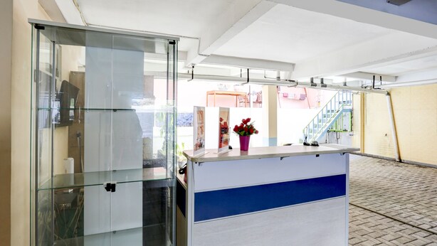 A reception desk with a glass partition and a blue stripe, a potted plant, and a staircase in the background. - OYO 4008 E Paviliun Karawaci (Curug)