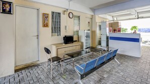 A waiting area with a reception desk, a clock, a television, a refrigerator, a chair, and a blue bench. - OYO 4008 E Paviliun Karawaci (Curug)