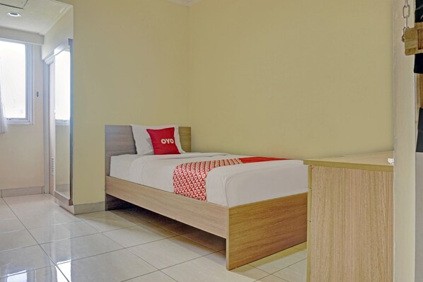 Una cama individual con estructura de madera, una colcha estampada en rojo y blanco, y una almohada roja con la palabra 'OYO'.
