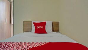 A hotel room with a bed, a red and white pillow with the word "OYO" on it, and a red and white patterned blanket. - OYO 4008 E Paviliun Karawaci (Curug)