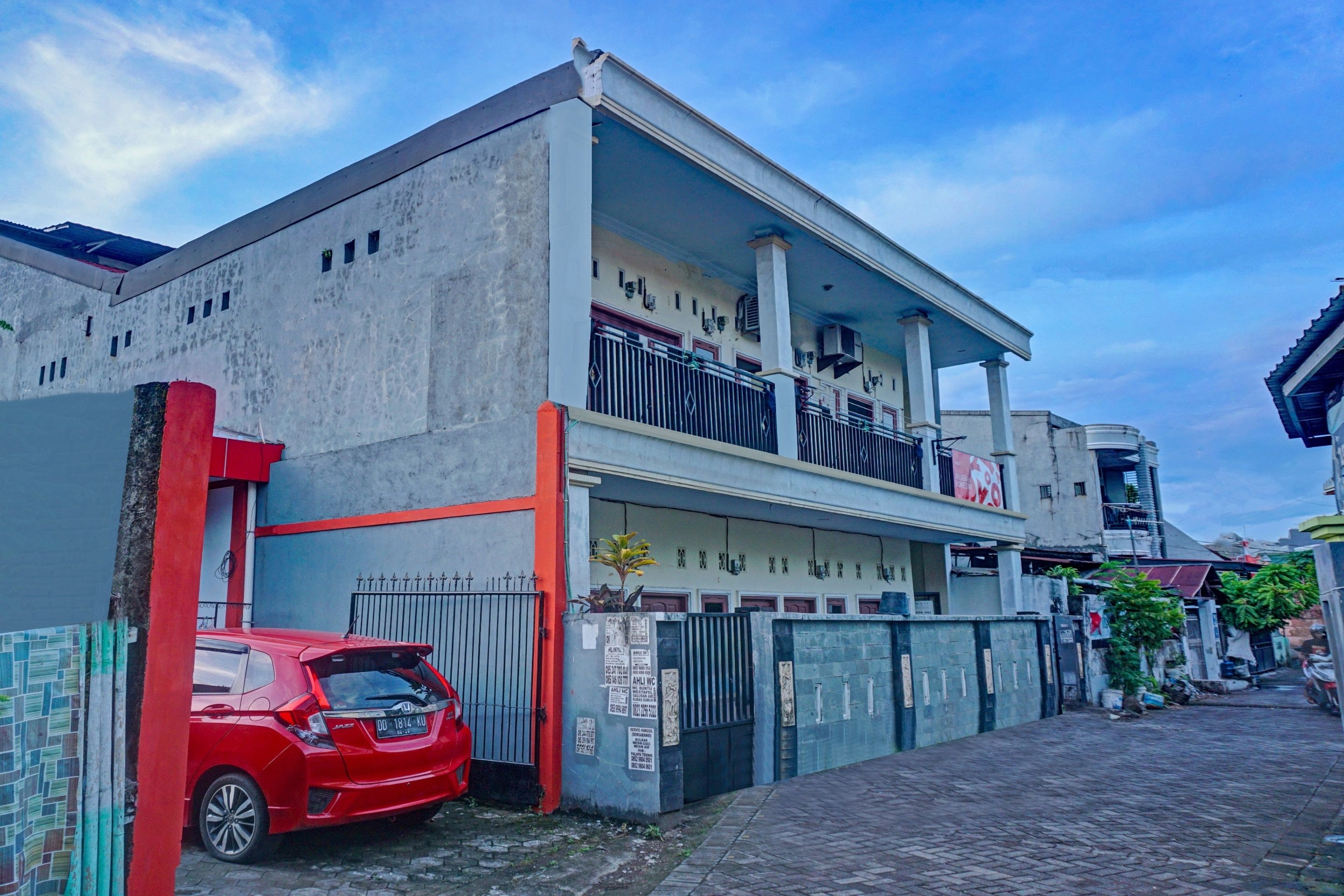 A two-story building with a balcony, a gated entrance, and a parked red car.