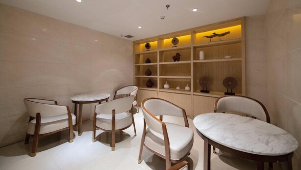 A modern interior with a seating area featuring four chairs and a marble-topped table, a wooden shelf unit with decorative items, and recessed ceiling lighting. - Ji Hotel Urumqi Youhao (Ürümqi)