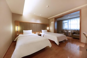 Quarto de hotel com duas camas, área de estar com um sofá e poltronas, e vista para o exterior.
