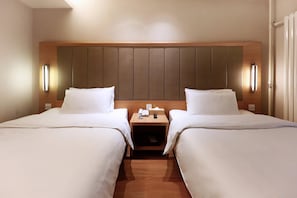 Quarto de hotel com duas camas, cabeceira de madeira, luminárias laterais e mesa de cabeceira com telefone e controle remoto.