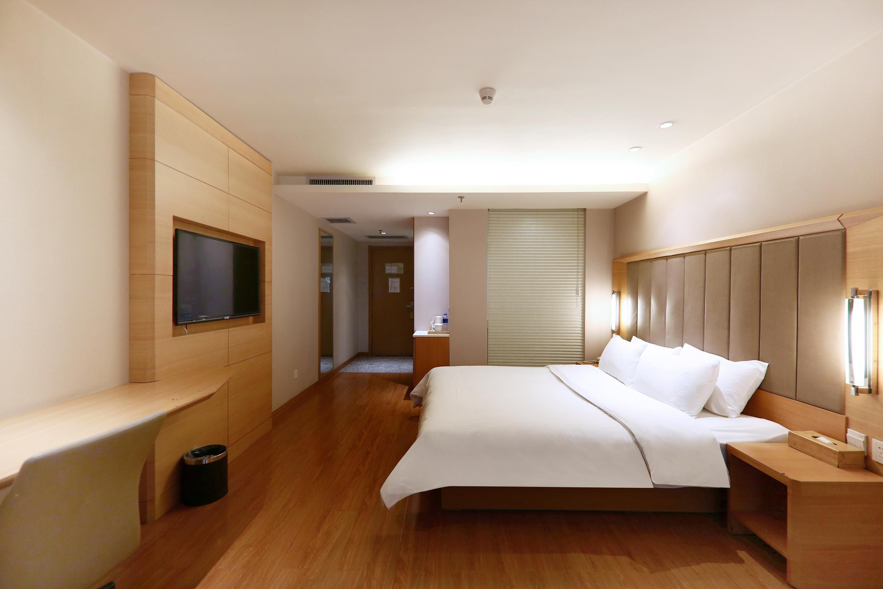 A hotel room with a bed, bedside tables, a TV mounted on the wall, and a window with blinds.