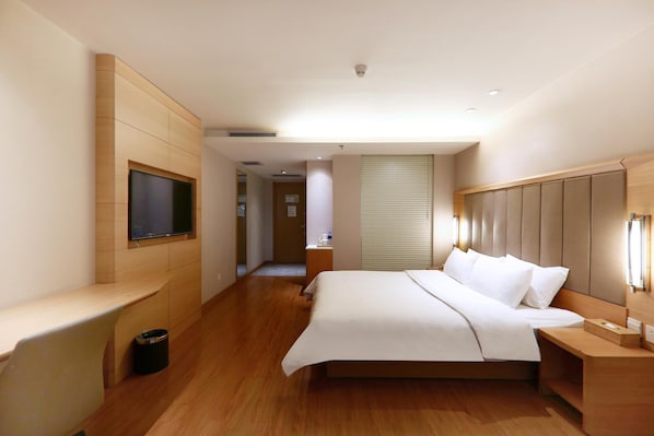 Quarto de hotel com cama, mesas de cabeceira, televisão fixada na parede e janela com persianas.