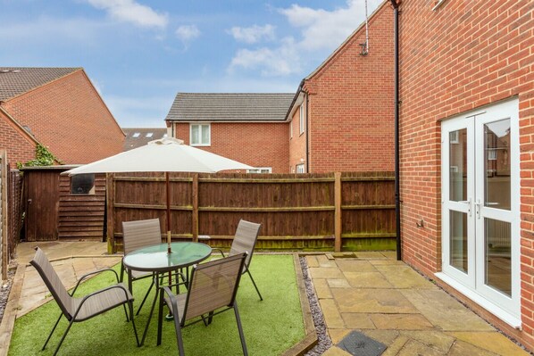 A patio with a table and chairs, a wooden fence, and a brick house with a glass door.