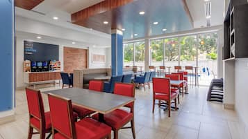 A modern coffee shop with a wooden ceiling, large windows, and red and blue seating areas.