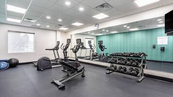 Un gimnasio con cintas de correr, elípticas y un estante con mancuernas.