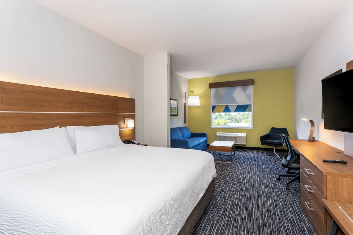 A hotel room with a large bed, a desk with a chair, a blue sofa, and a TV.