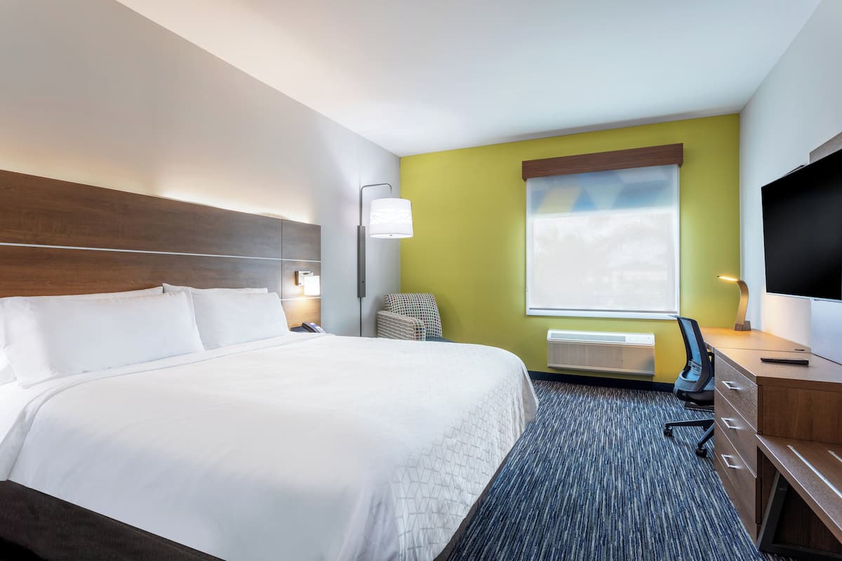 A hotel room with a large bed, a desk with a chair, a flat-screen TV, a lamp, and a window with a view.