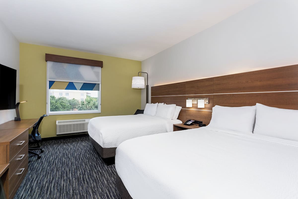 A hotel room with two beds, a desk, a chair, a TV, a window with a view, and a lamp.