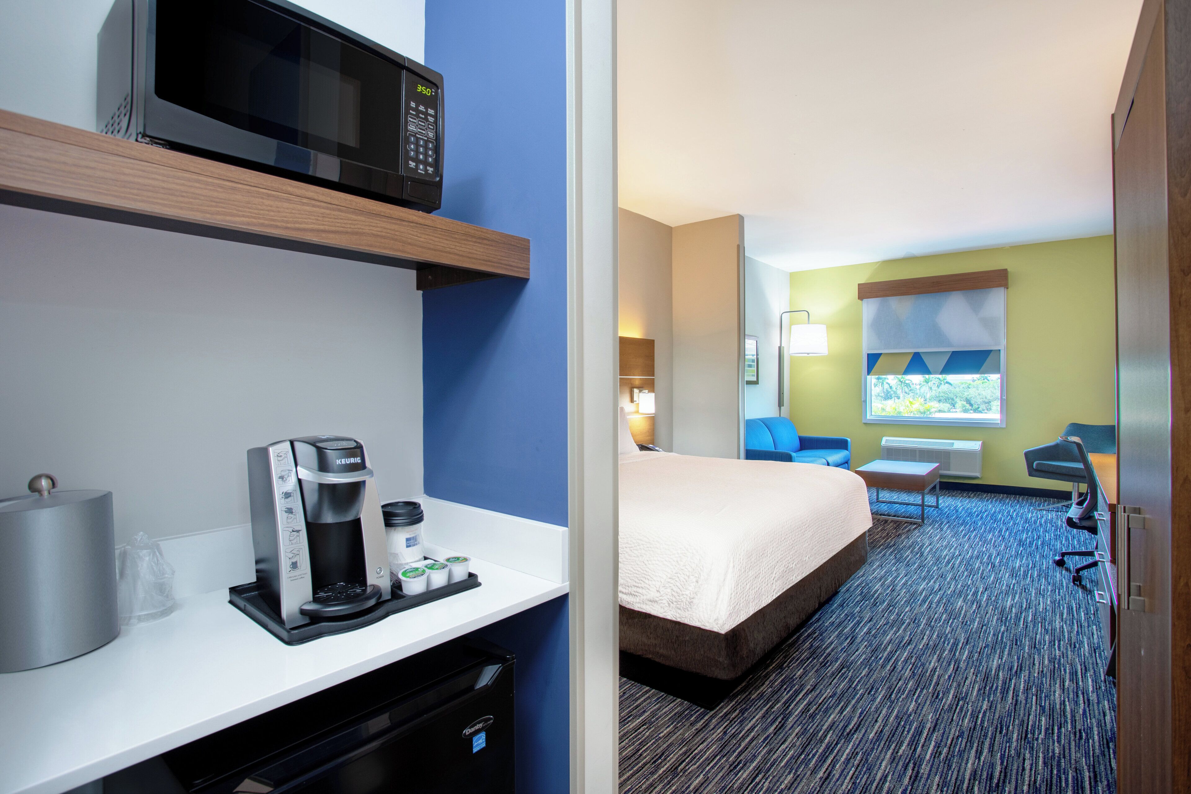 A hotel room with a bed, a desk with a coffee maker, a microwave, and a window with a view.