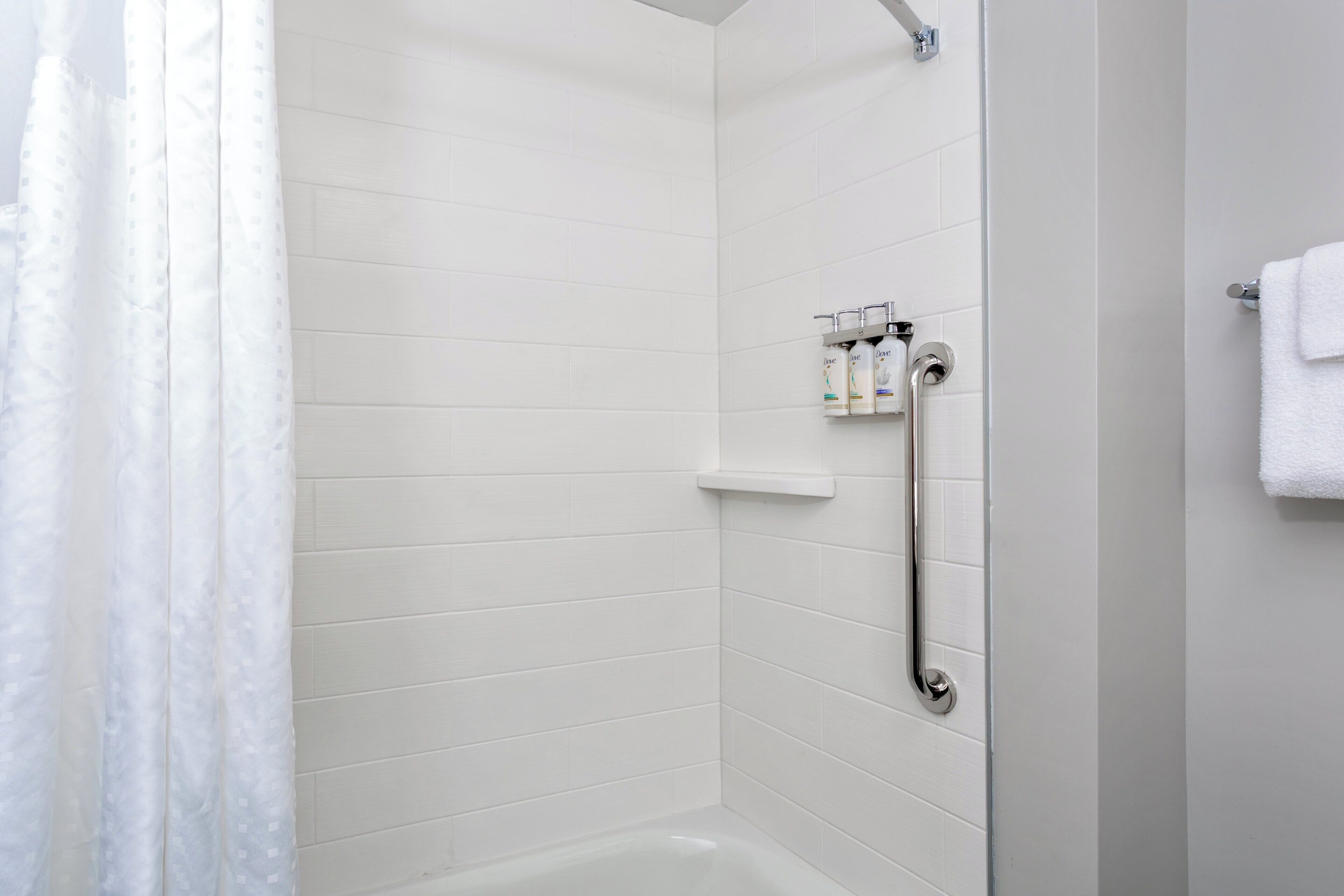 Une salle de bain moderne avec des murs recouverts de carreaux blancs, un espace douche et un porte-serviettes.