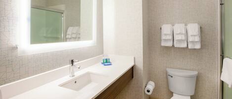 A bathroom with a white sink, mirror, and toilet. There are towels hanging on the wall.