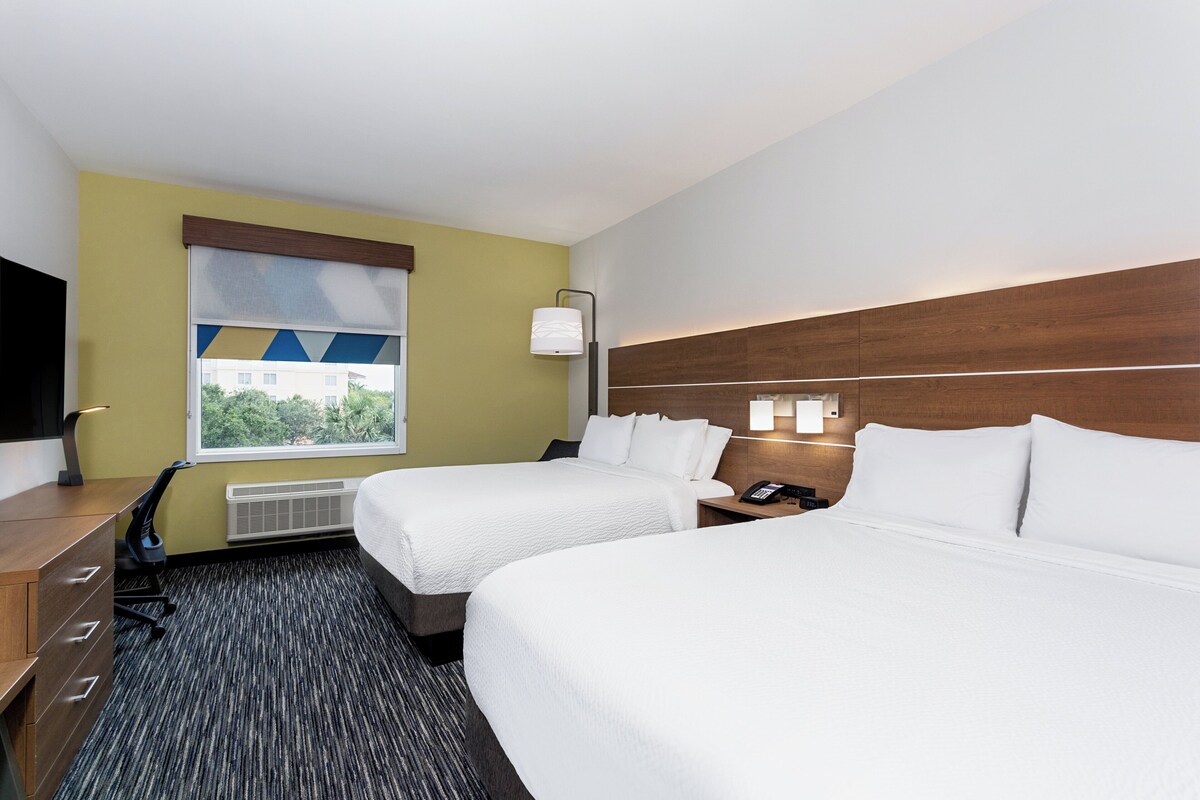 Une chambre d’hôtel avec deux lits, un bureau, une chaise, une télévision, une fenêtre donnant sur un beau paysage et une lampe.