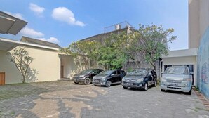 A paved courtyard with four cars parked in a row, a building with a flat roof, and a tree with yellow flowers. - OYO Capital O 90410 Griya Amanah Jajar Syariah (Surakarta)