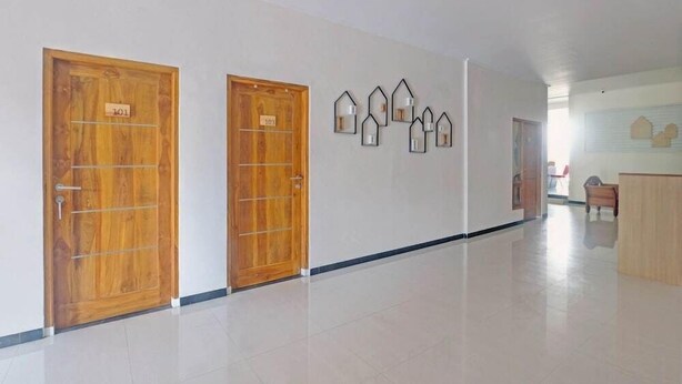 A hallway with two wooden doors labeled 101 and 103, a row of wall-mounted light fixtures, and a reception desk in the distance. - OYO Capital O 90410 Griya Amanah Jajar Syariah (Surakarta)