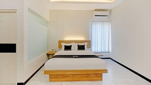 A modern hotel room with a large bed, a bedside table, a nightstand, and an air conditioning unit. - OYO Capital O 90410 Griya Amanah Jajar Syariah (Surakarta)