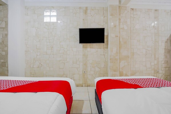 A hotel room with two beds, each with a red and white patterned bedspread, and a flat-screen TV mounted on the wall.