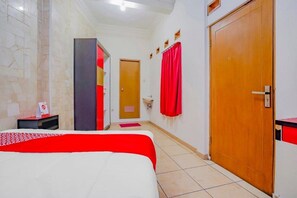 A hotel room with a bed, a wooden door, a bathroom with a mirror, and a red curtain.