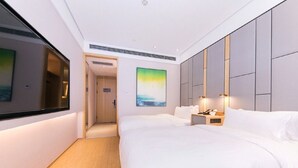 A modern hotel room with a large bed, bedside tables, a painting, and a view through a window. - Ji Hotel (Shanghai)