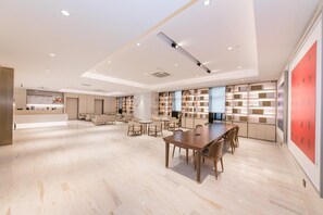 A spacious hotel lobby with a reception desk, seating area, and a large dining table.